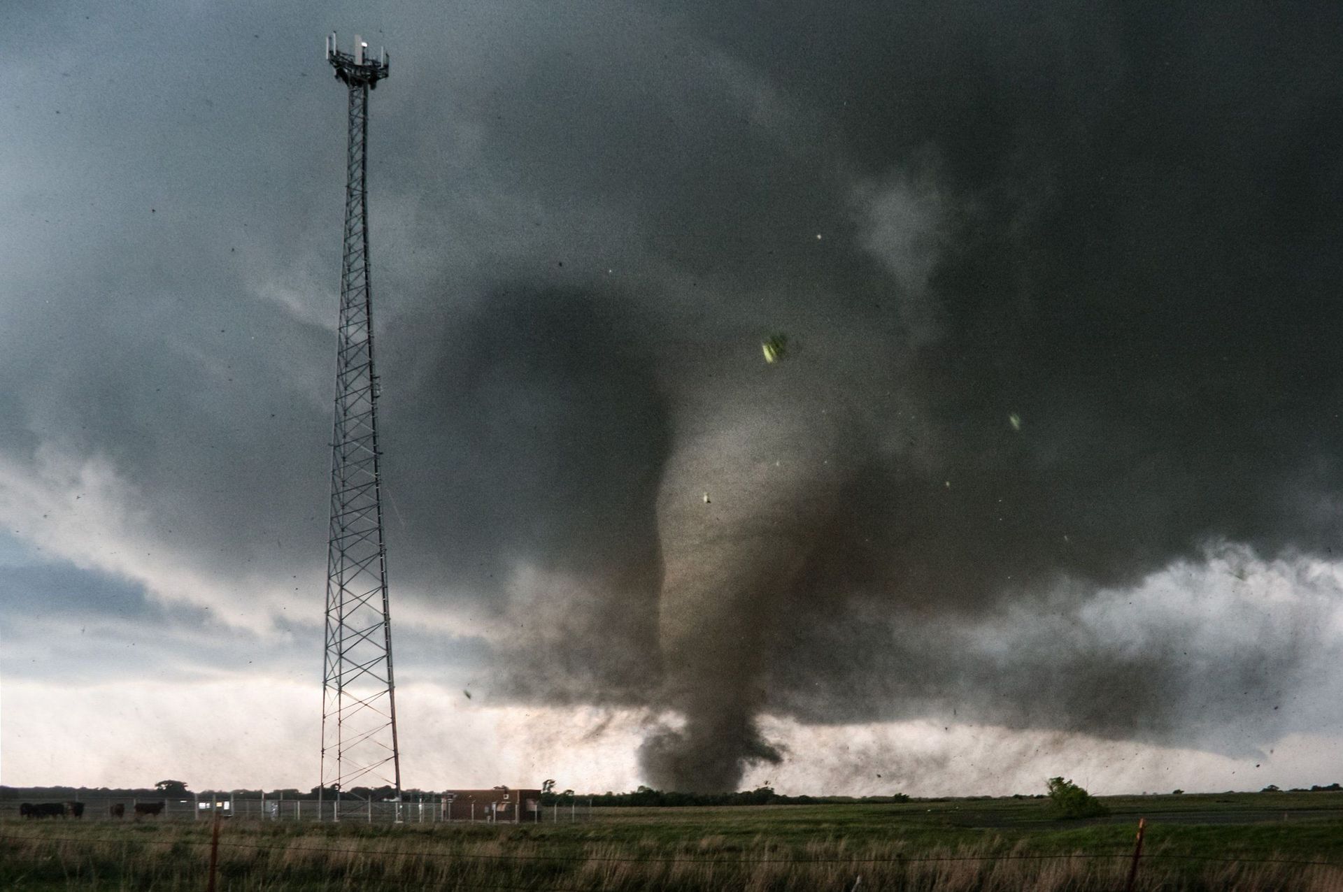 A tornado is moving through a field with a tower in the foreground.