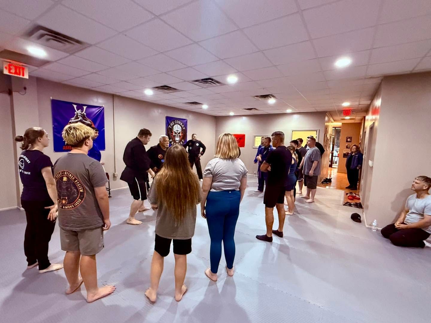 People standing barefoot in a hallway during a group activity or class, with chairs along the walls.
