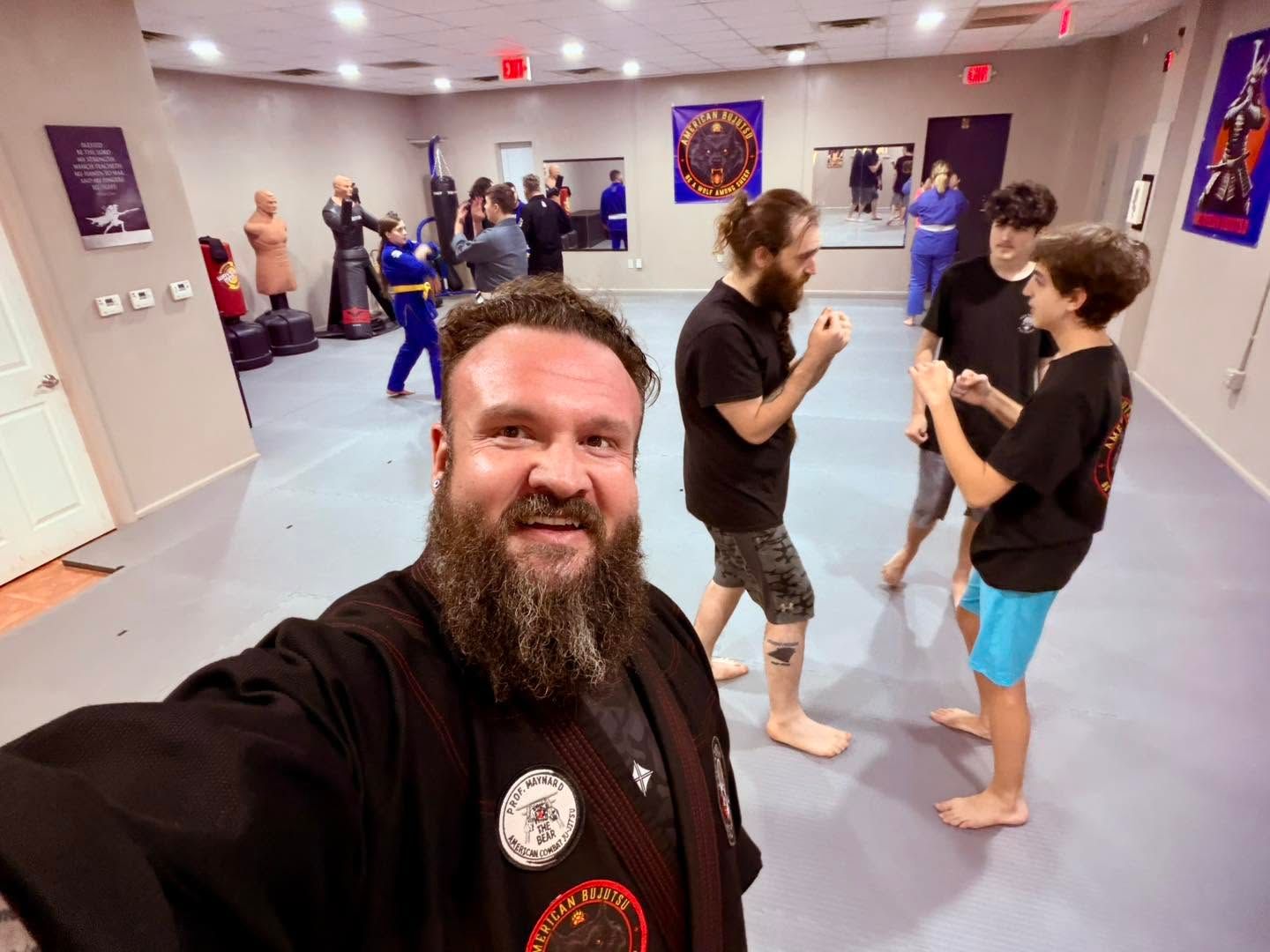 Selfie in a martial arts studio with people practicing and chatting in the background.