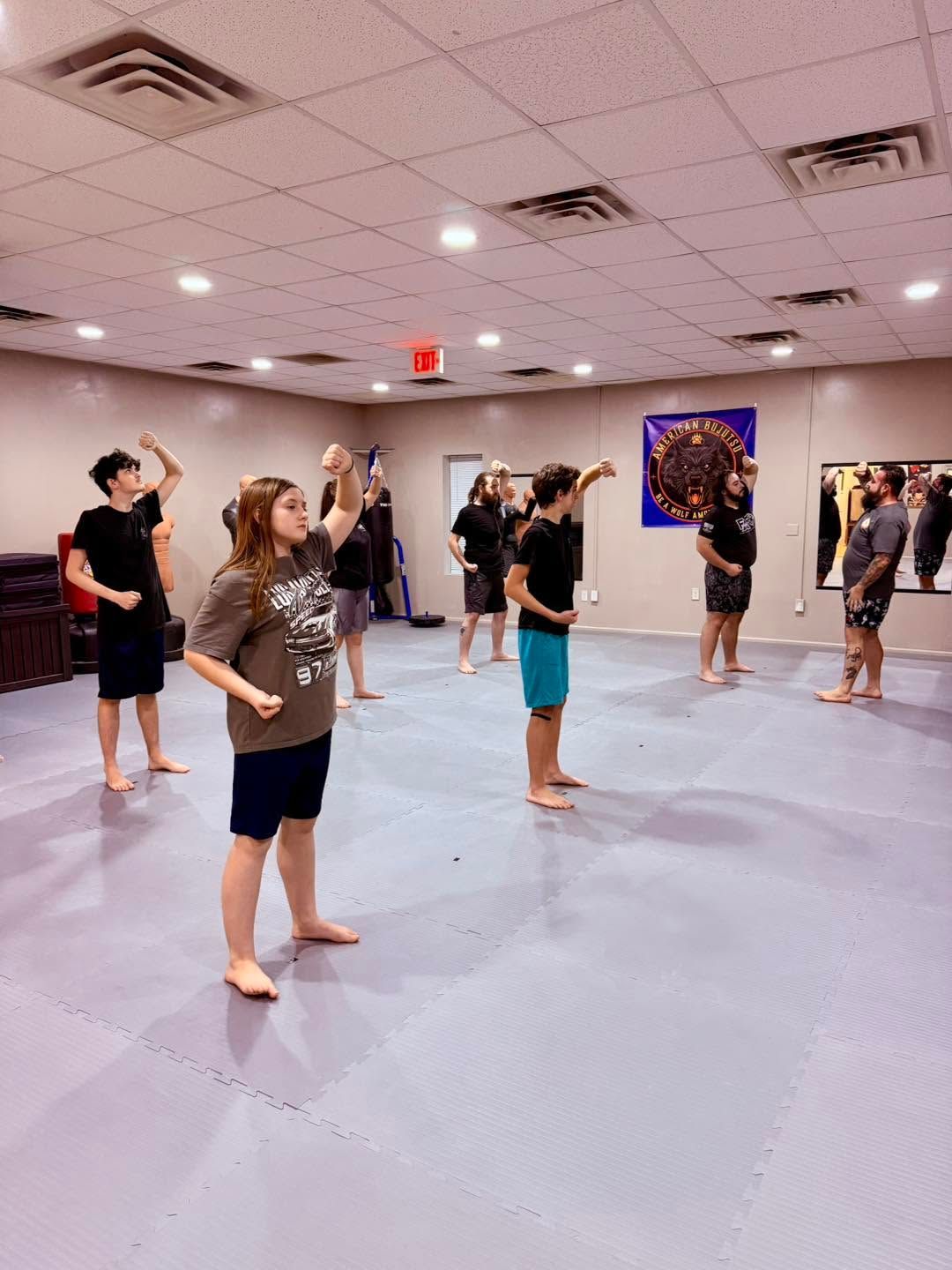 People standing in a dance studio, practicing with arms raised on a light blue floor.