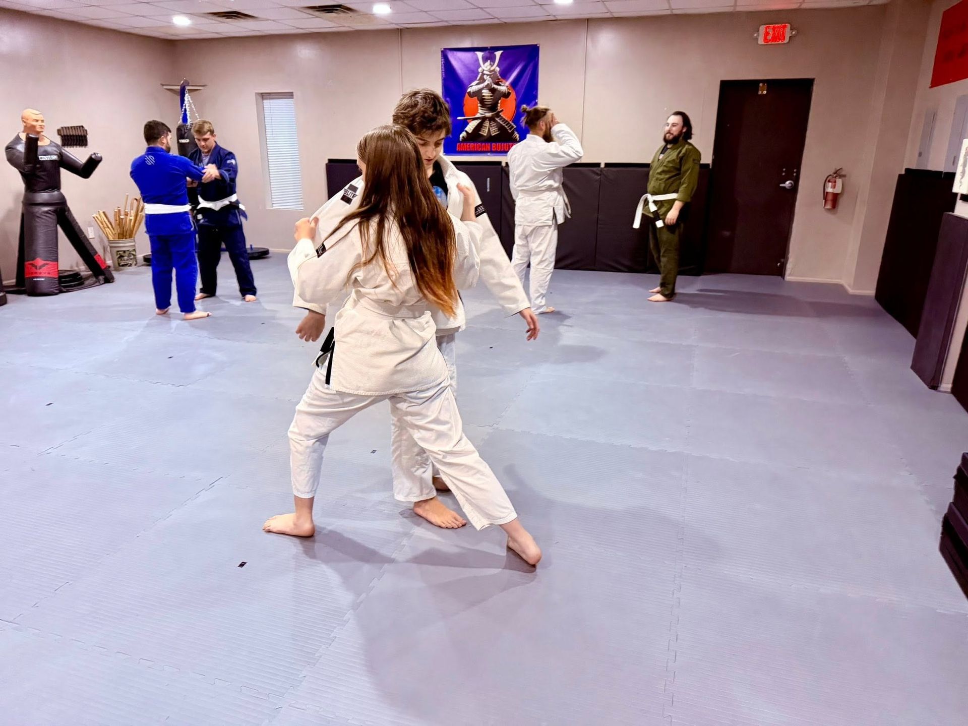 People practicing martial arts in a studio with blue mats and wall mirrors