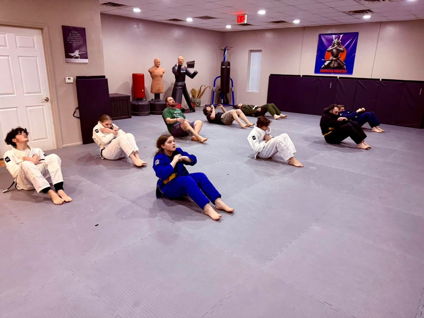 Group exercise class in a studio, people seated on mats doing a core workout.