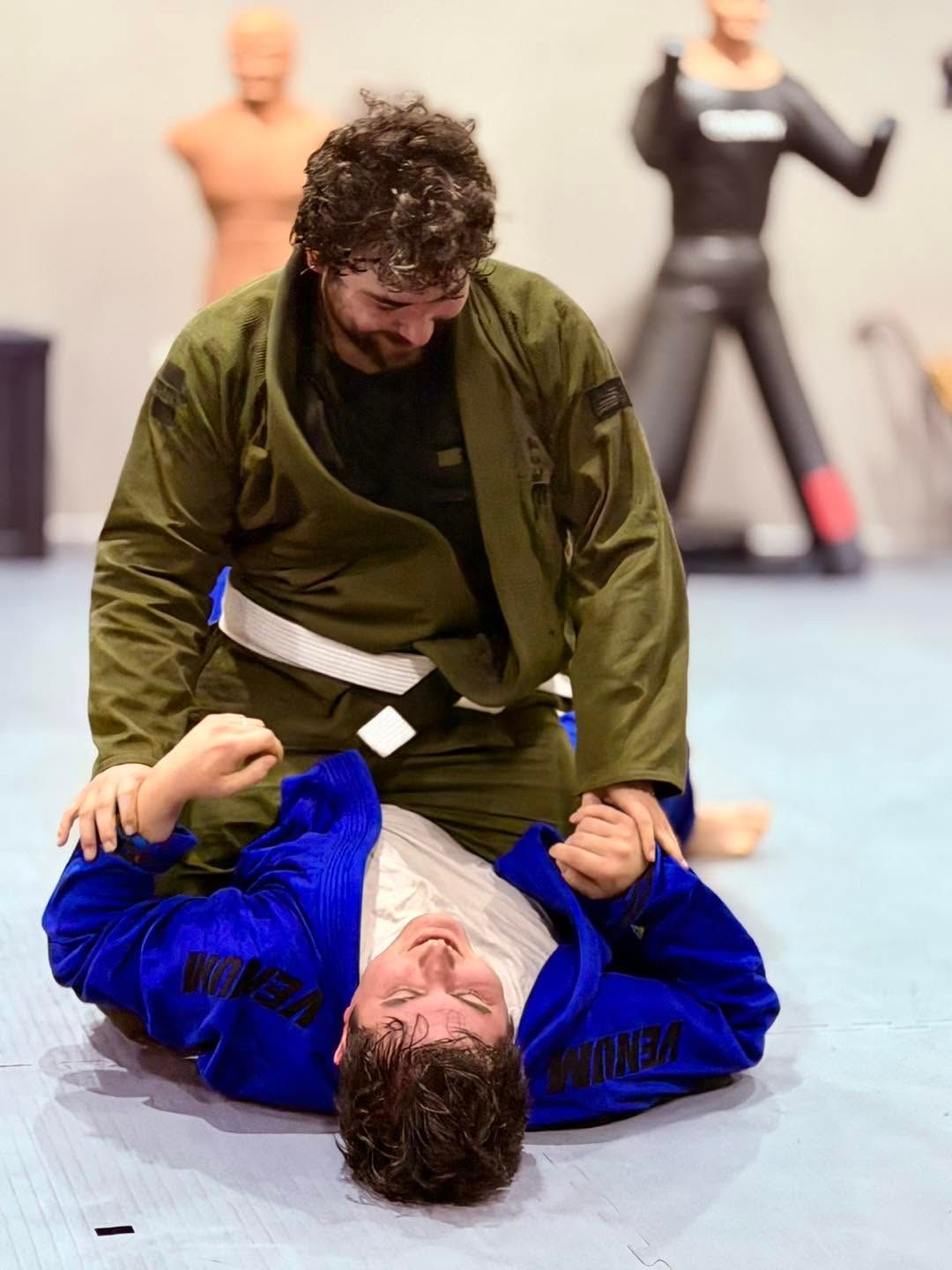 Jiu-jitsu training drill with one man holding another in a grappling position on a mat.