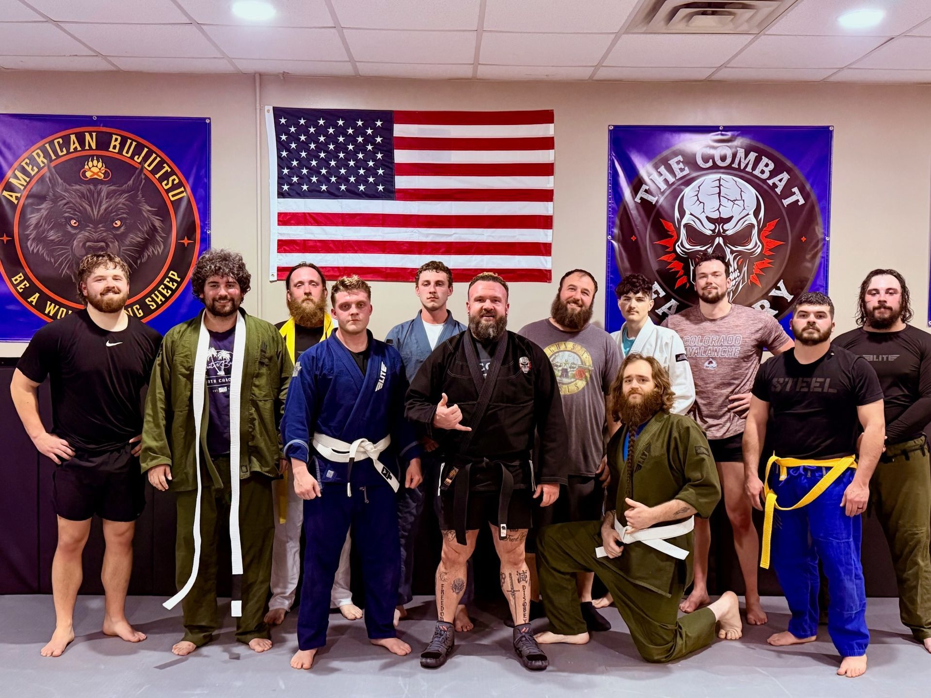 Group photo of martial artists posing barefoot indoors in front of a U.S. flag and academy banners