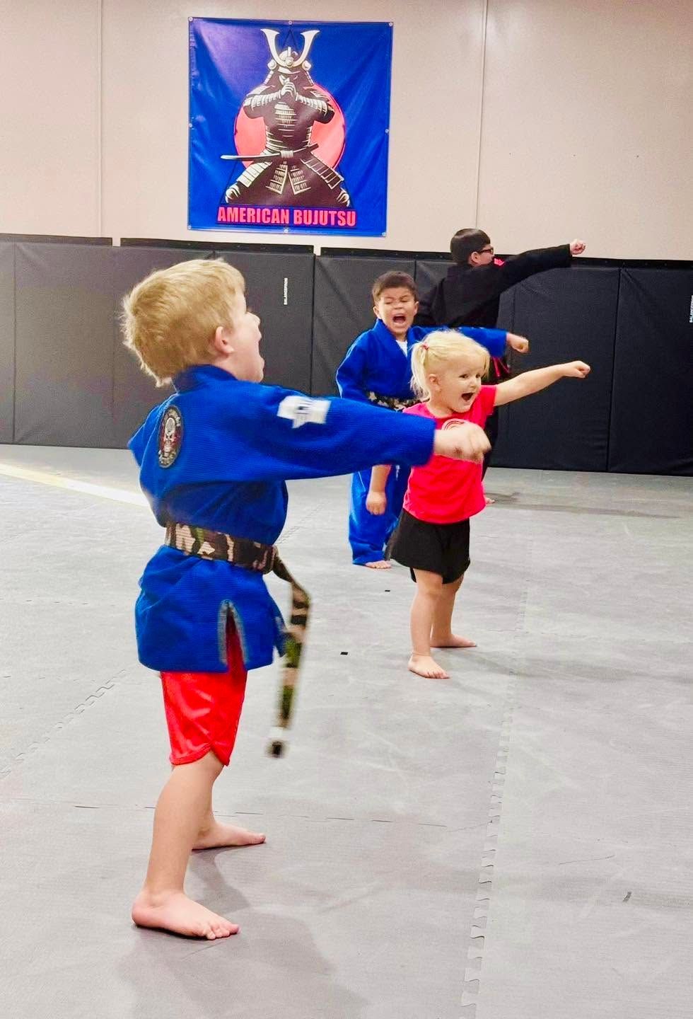 Children in martial arts uniforms practice punches in a gym