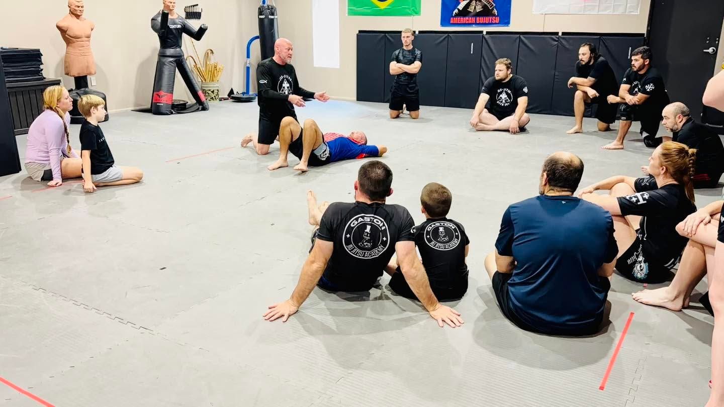 Group seated on floor in a martial arts class, facing an instructor in a studio.