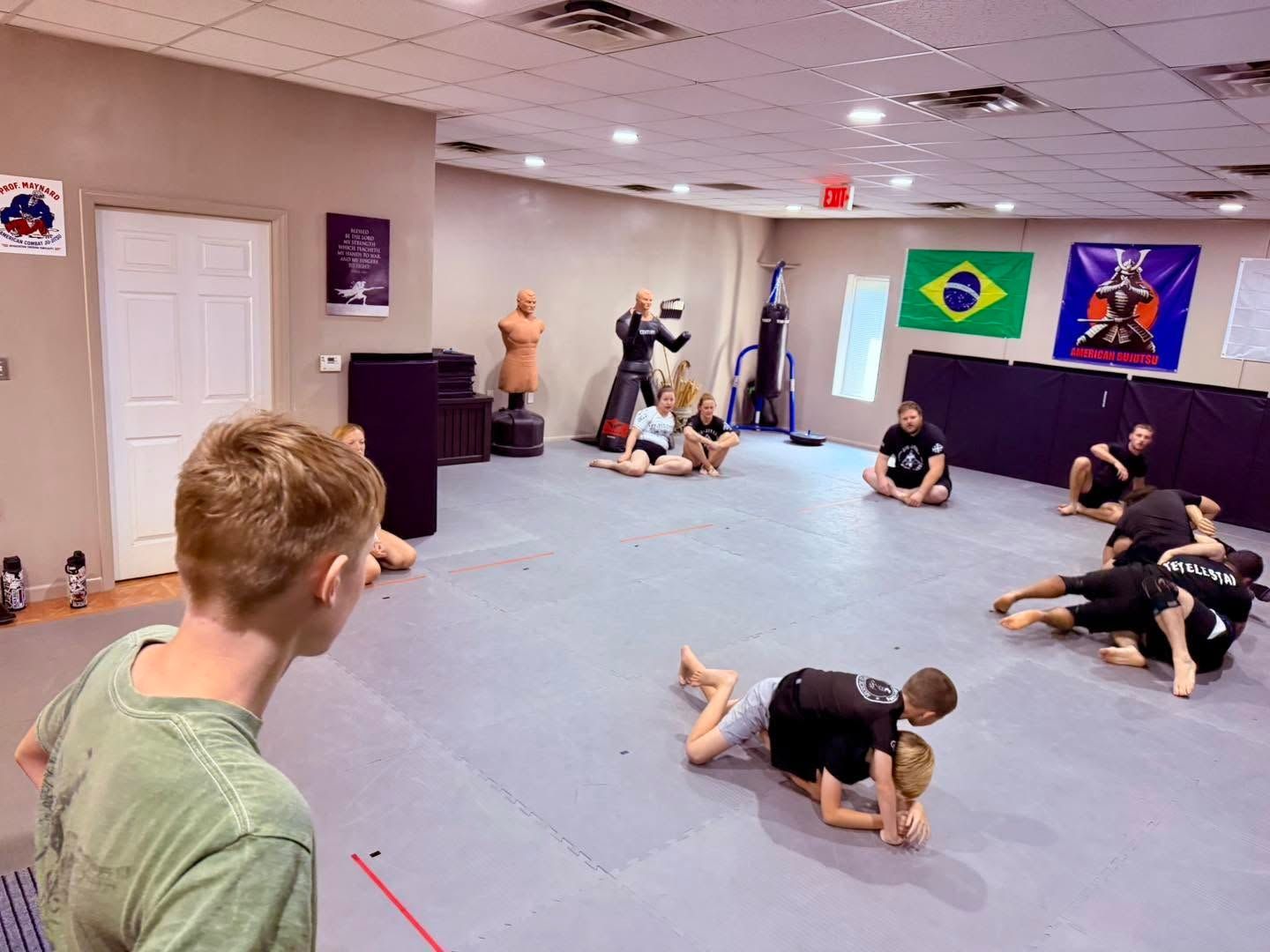 Martial arts class practicing grappling drills on padded mats in a studio with Brazilian flags on the wall