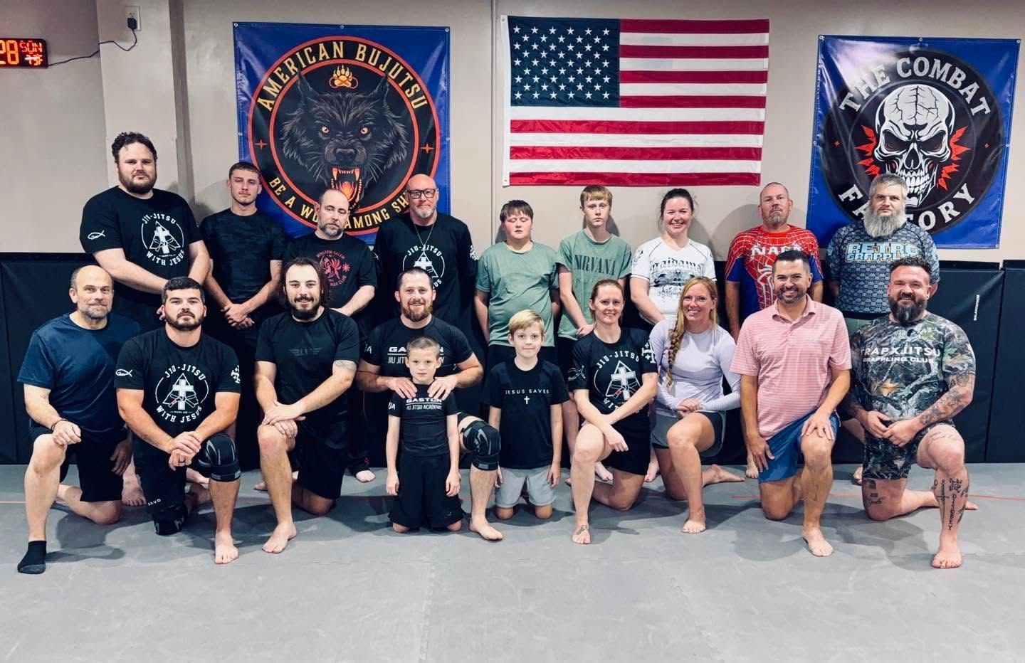 Group posing in a gym in front of banners and a U.S. flag, holding trophies and wearing team shirts