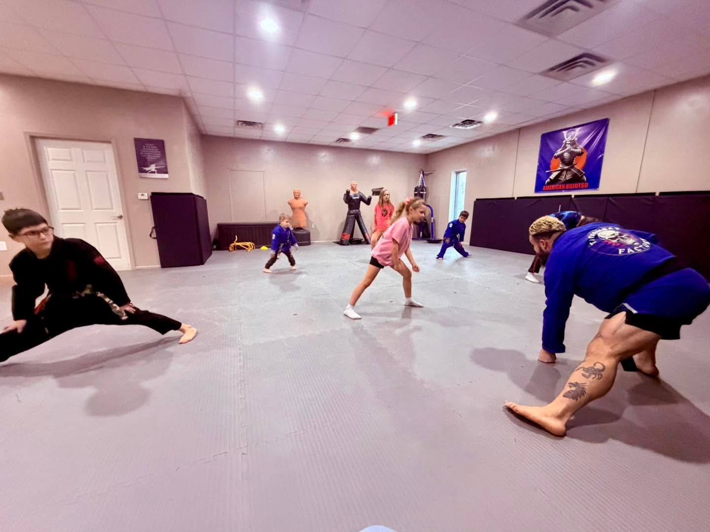 People stretching on mats in a martial arts or fitness studio with purple walls and overhead lights