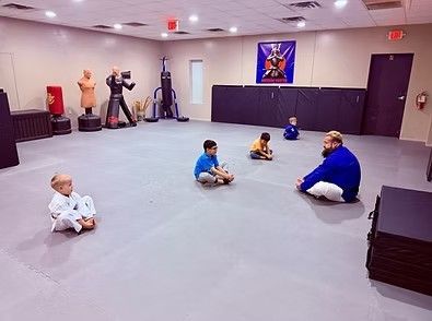 Children and an instructor sit on a mats floor in a martial arts studio