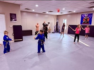 Children in blue uniforms practicing martial arts in a studio with mirrors and mats.