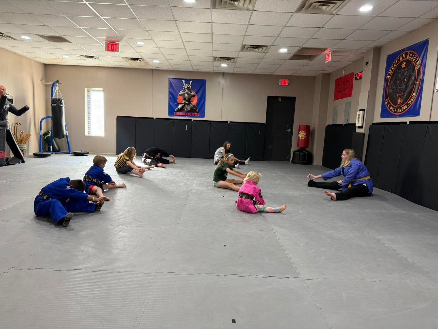 People stretching on a gray mat in a martial arts studio with banners on the walls