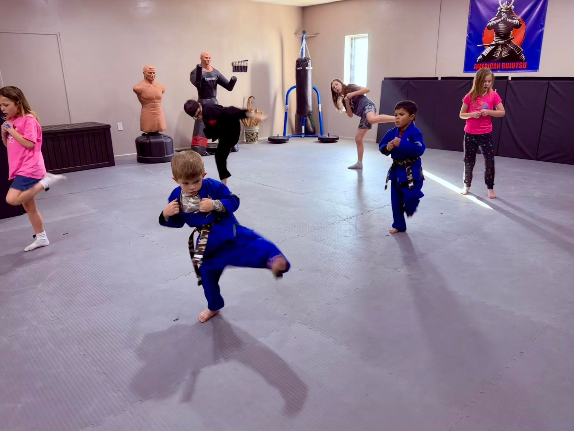 Children practicing martial arts in a studio, wearing blue uniforms and kicking in formation