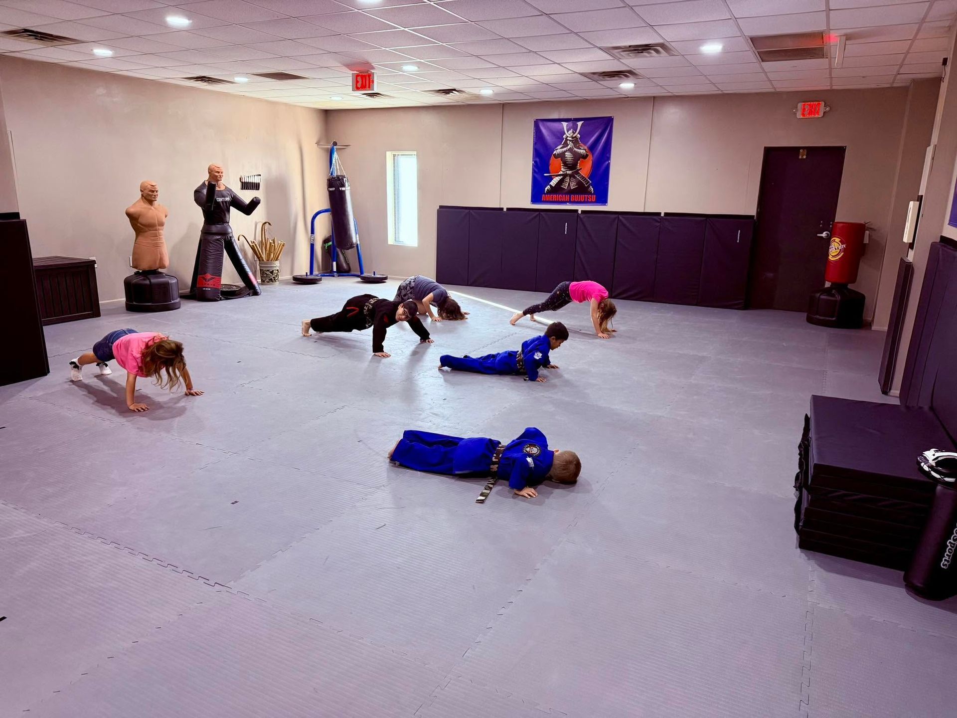 People doing floor exercises in a martial arts studio with mats and training equipment