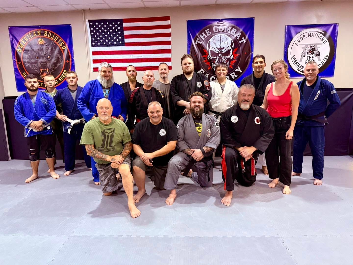 Group of martial arts practitioners posing in gis and uniforms before flags and academy banners