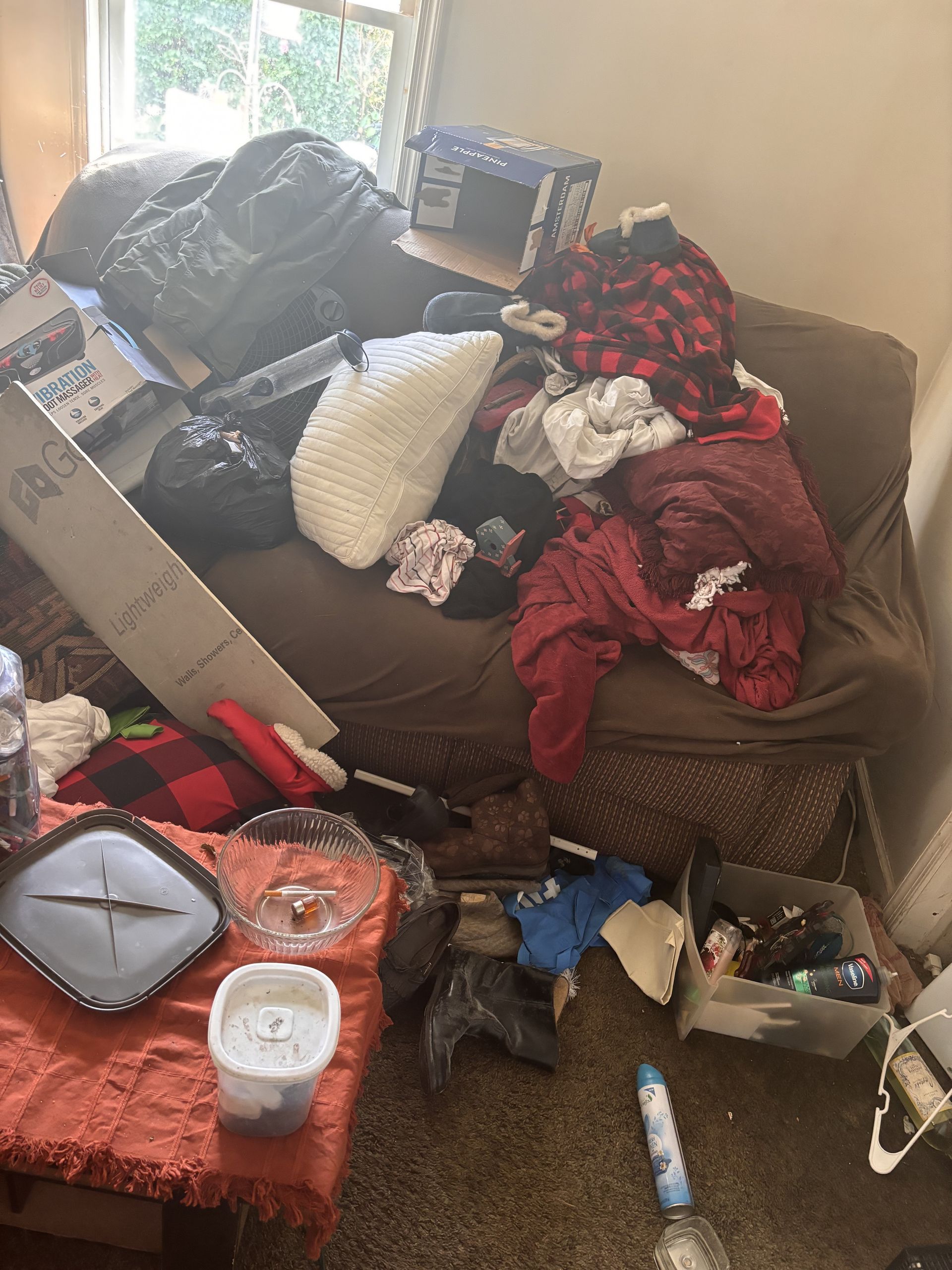 A messy room with a bed , couch , table and clock.