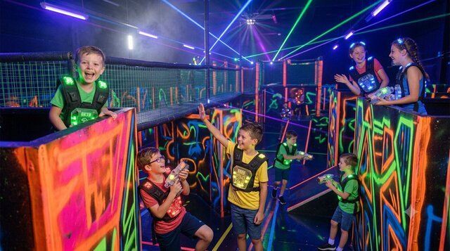 energetic and playful children playing laser tag in a neon-lit maze wear glowing vests and hold laser guns smiling and laughing under vibrant colorful lights