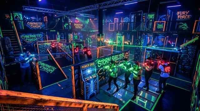 several players engaged in a laser tag game illuminated by colorful lights in a dark environment