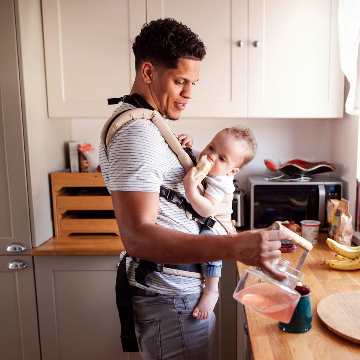 A man is holding a baby in a carrier in a kitchen.
