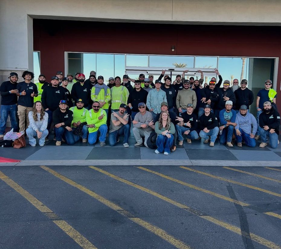 Large group posing outside a building, with a red awning and yellow parking lines in front
