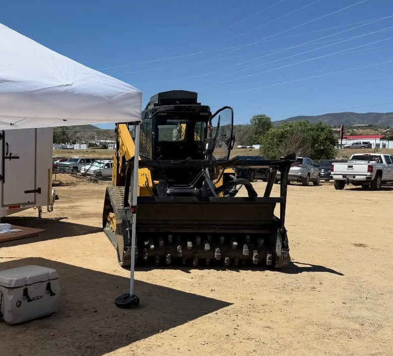 Off-road vehicle with crawler attachment parked at an outdoor event under a white canopy.