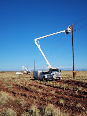 Utility truck with boom lift working on power lines in a dry field under a clear blue sky