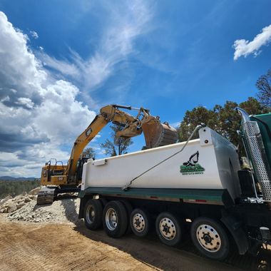 Excavator loading debris into a white dump truck under a blue sky