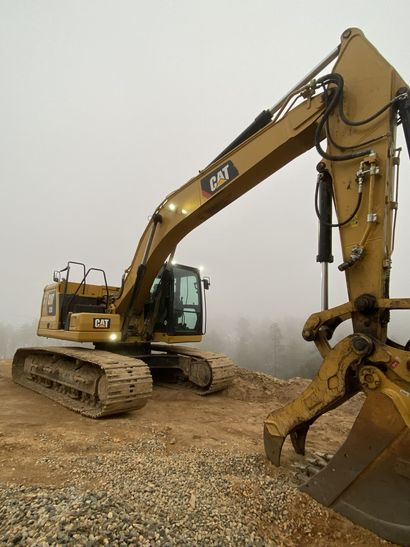 Yellow excavator on a muddy construction site, viewed close-up with its bucket raised.