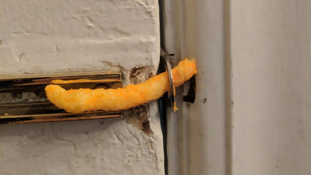 A close up of a door handle with a cheetos sticking out of it.