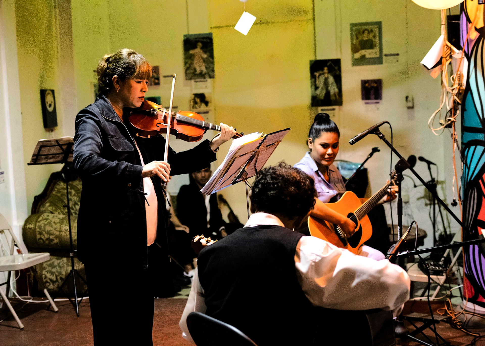 Dos músicos ensayan violín en una sala de estar; uno toca mientras el otro dirige.