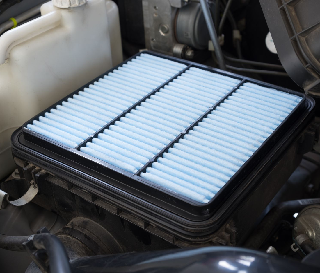 Filtro aria motore per auto con pannello plissettato bianco in una cornice nera, montato nel vano motore.
