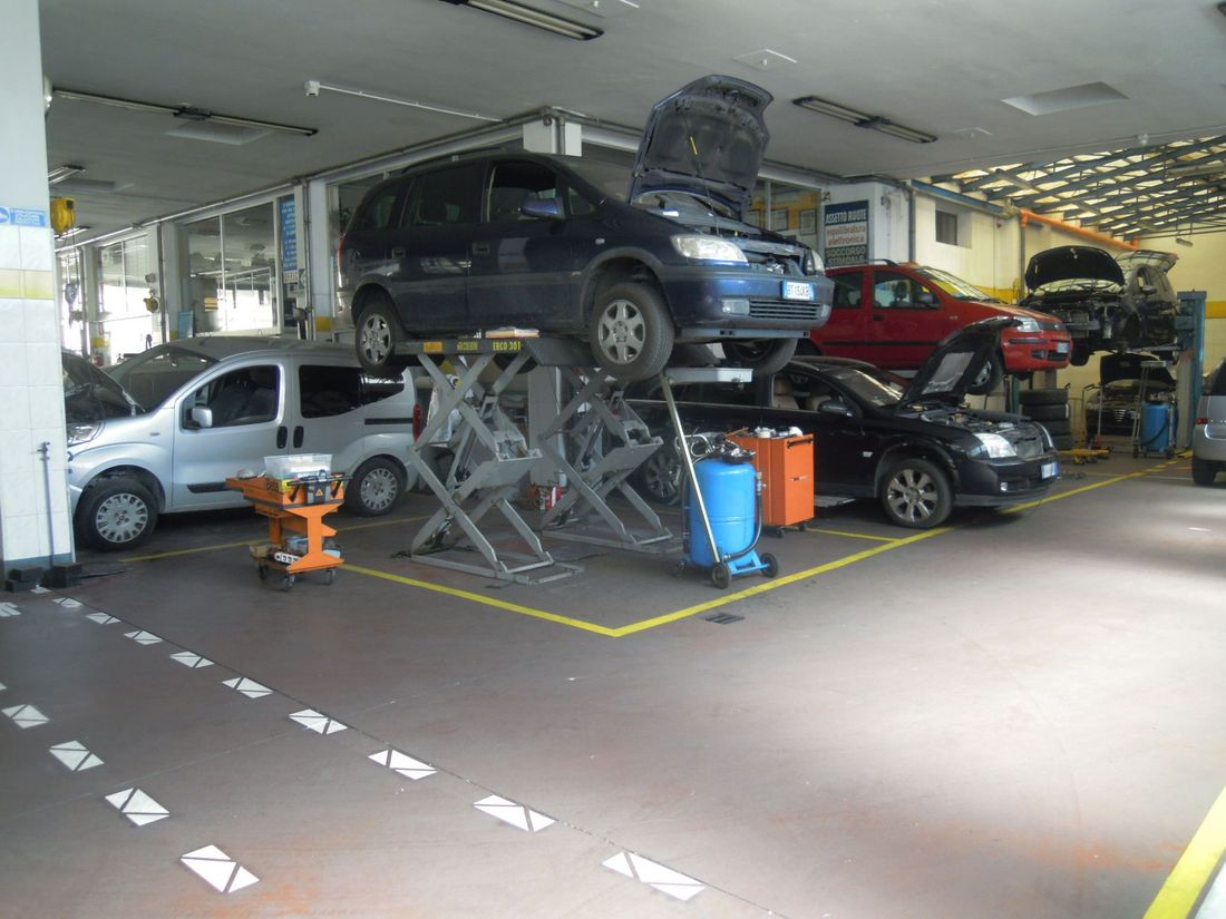 Officina automobilistica con diverse auto impilate su sollevatori idraulici all'interno di un garage.