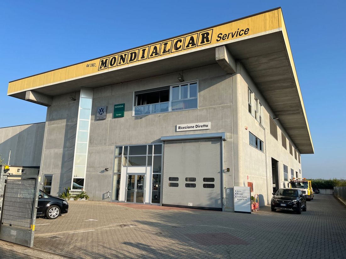Moderno edificio di servizio in cemento con ampio tetto aggettante e auto parcheggiate all'esterno.