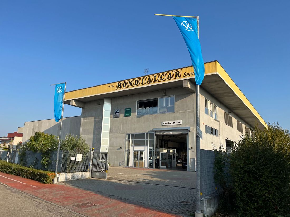 Ingresso di un edificio moderno con bandiere blu e tetto giallo sotto un cielo limpido.
