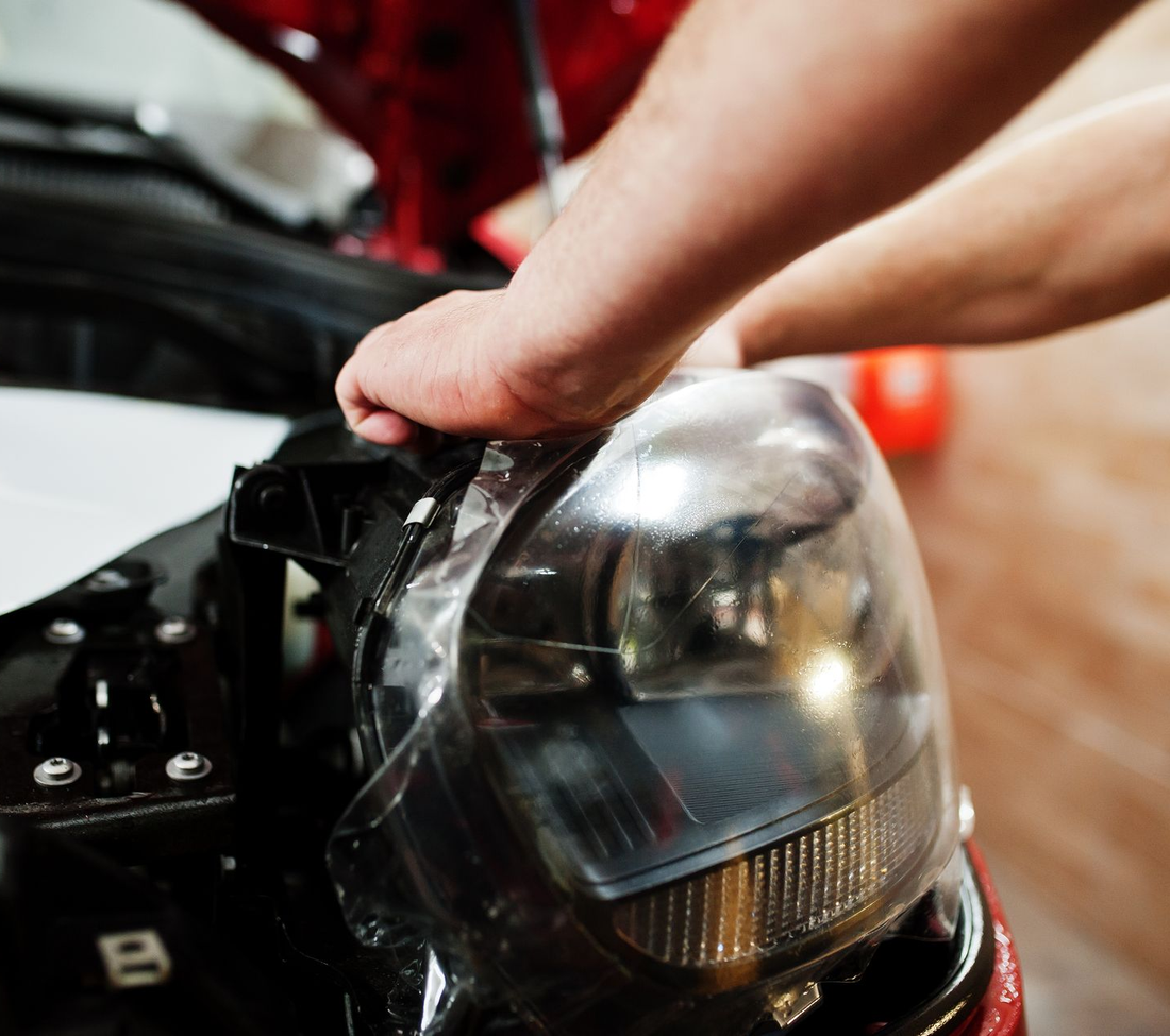 Mani che avvolgono una pellicola di plastica trasparente attorno al faro di una motocicletta in un garage