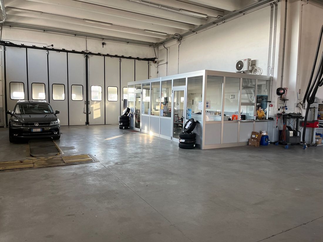 Ampia officina meccanica con un'auto nera, un ufficio con pareti in vetro e attrezzature di servizio all'interno.