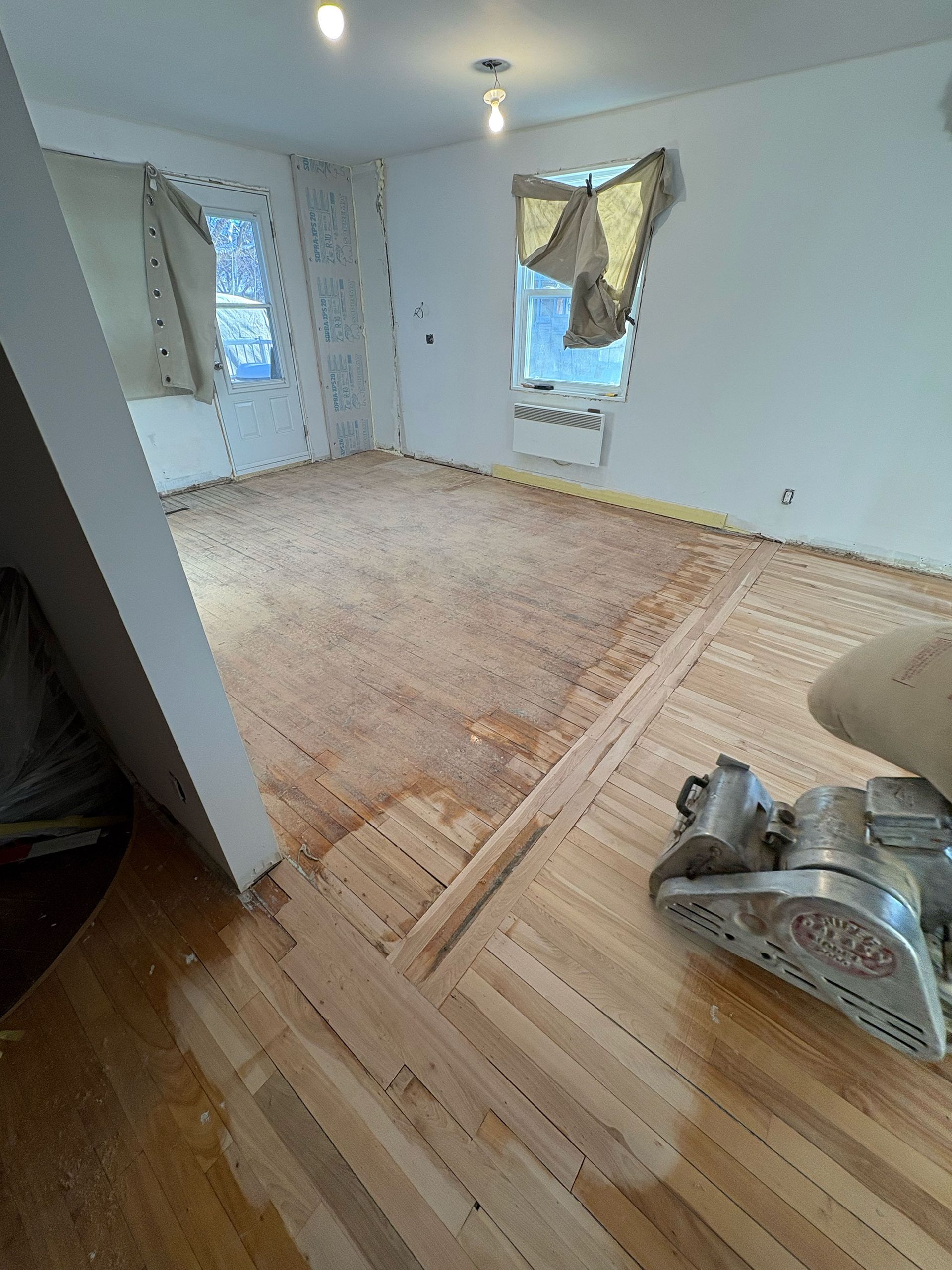 Une personne ponce un plancher en bois dans une pièce.