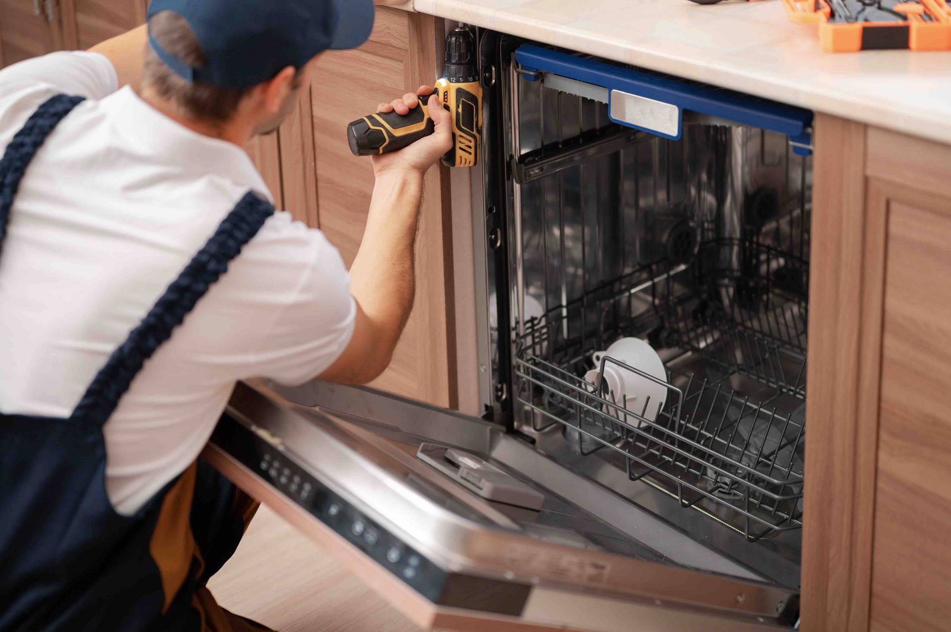 Person using a drill to repair an open dishwasher in a kitchen