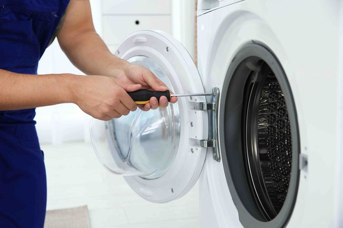 Technician using a screwdriver to repair an open washing machine door