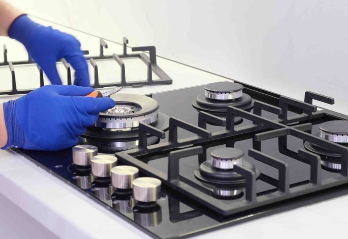Blue-gloved hands adjusting a stainless steel gas stove burner on a black cooktop
