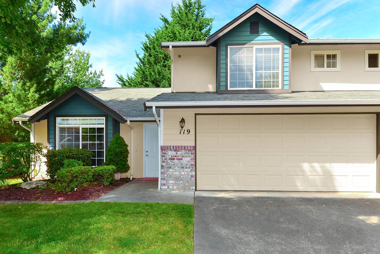 Exterior view of a townhouse-style multifamily building with a two-car garage, front door, and landscaped yard.