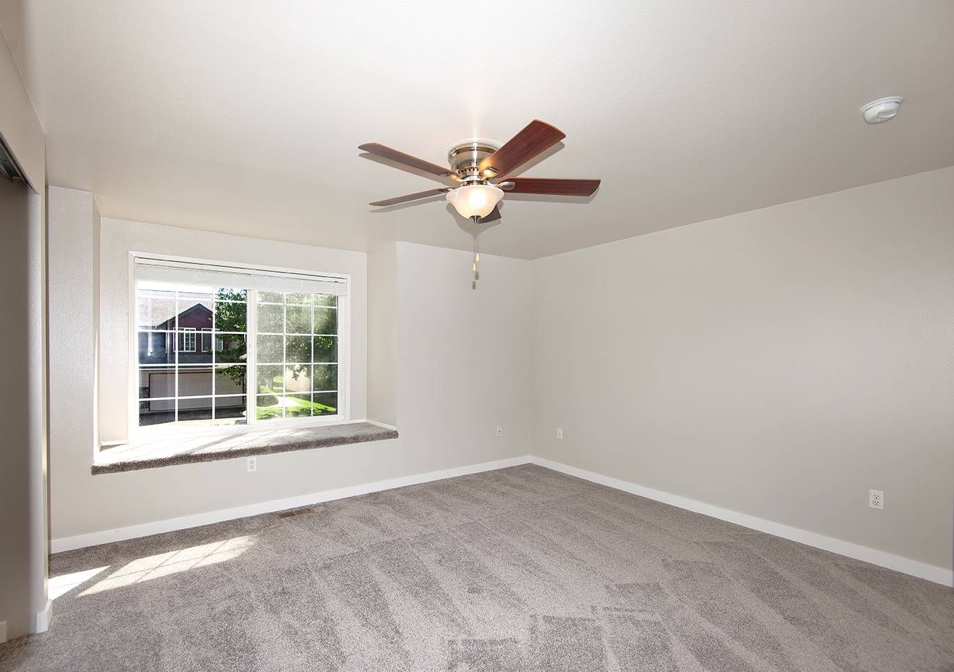Empty bedroom with a large window, carpet, and ceiling fan.