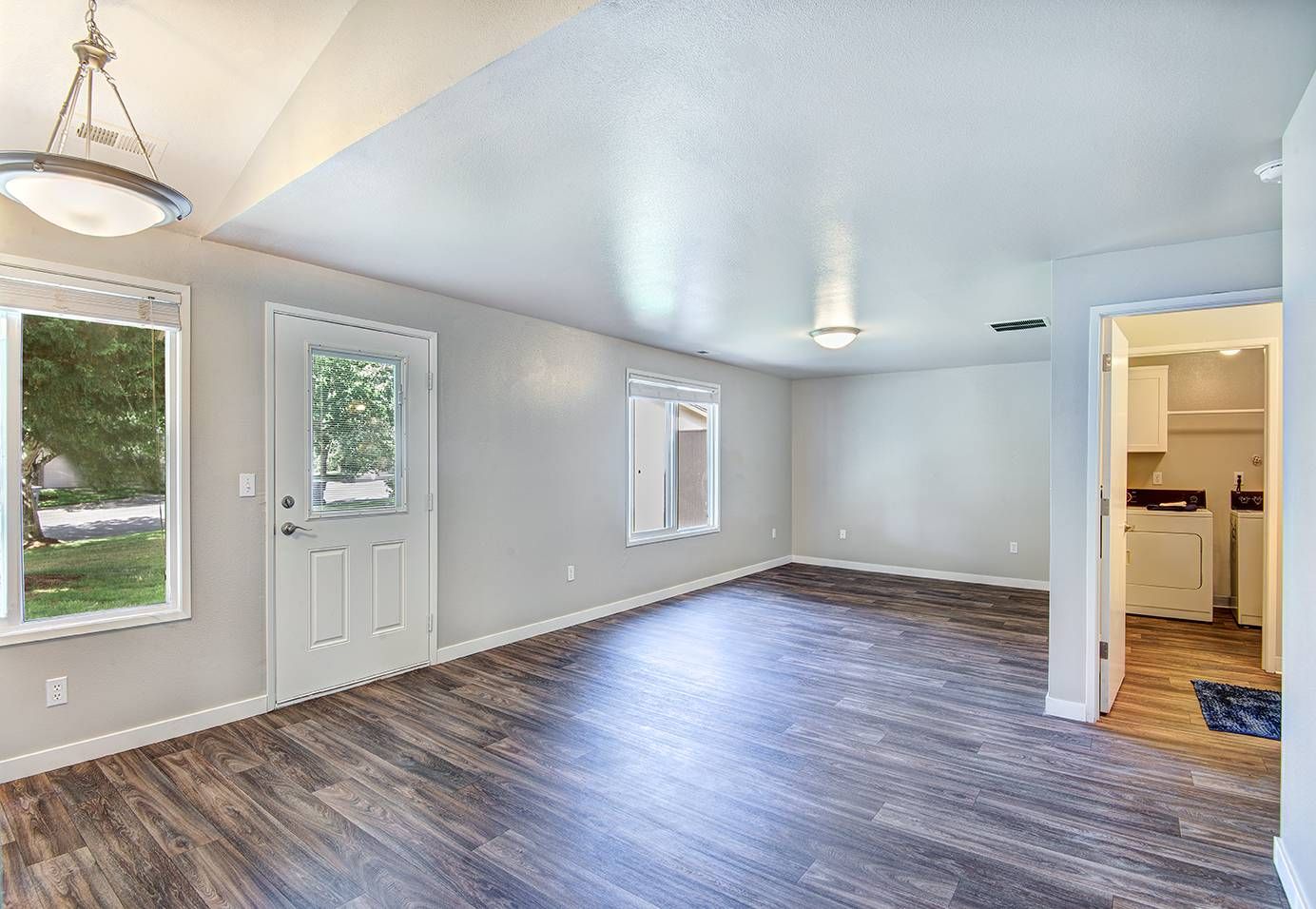 Living room with gray walls, wood-look flooring, a door to outside, and a visible laundry area.