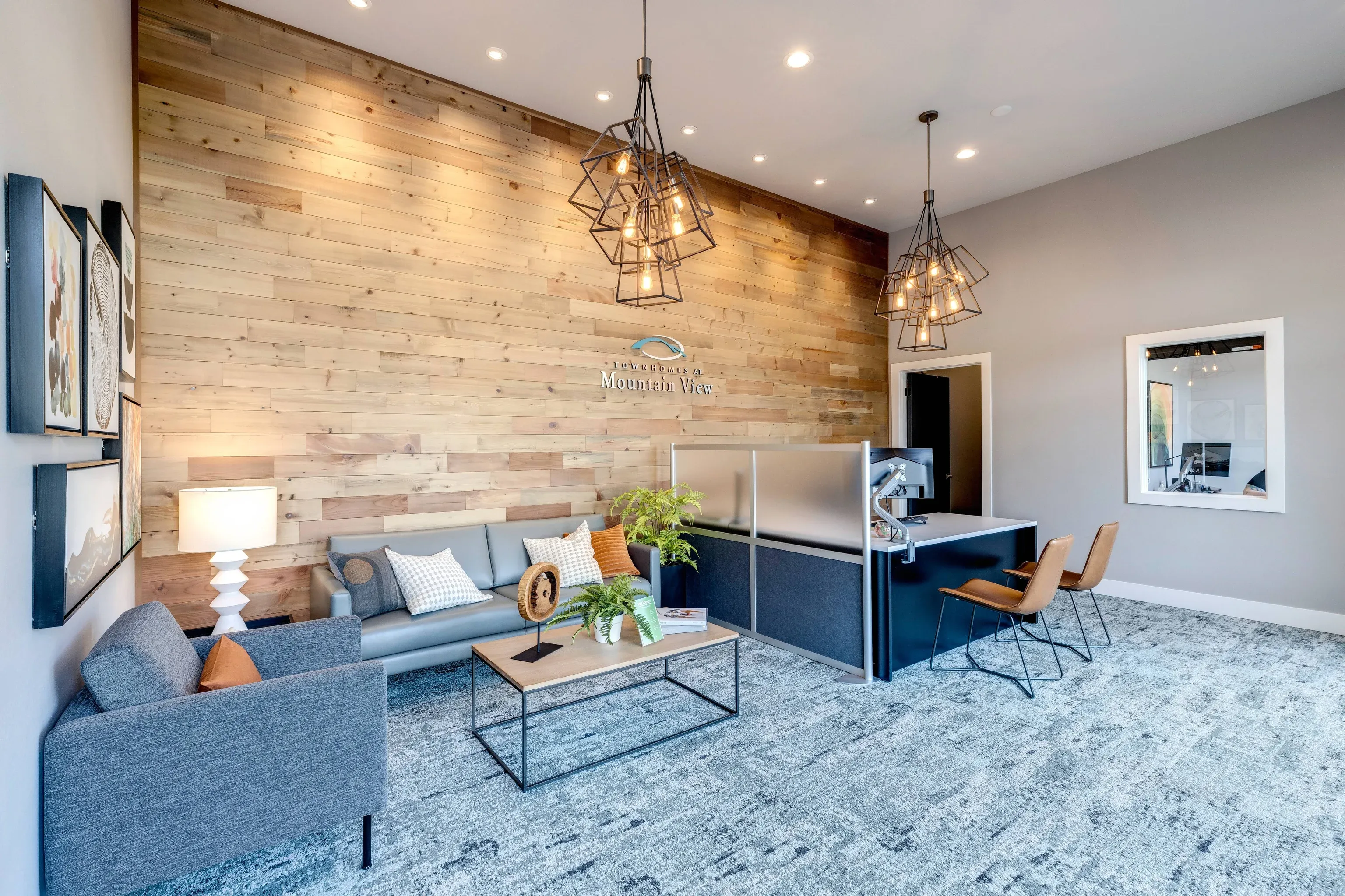 Leasing office lobby with a wood accent wall, sofa, coffee table, plants, and geometric pendant lights.