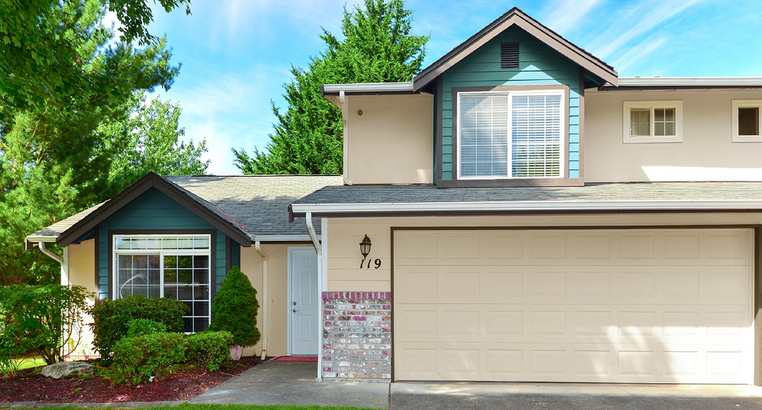 Beige two-story Apartment with green accents, garage, and front door; trees and blue sky background.