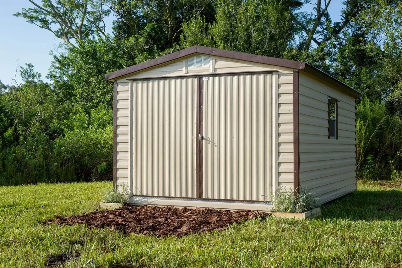 Tan shed with corrugated doors and small window, set in a grassy yard.