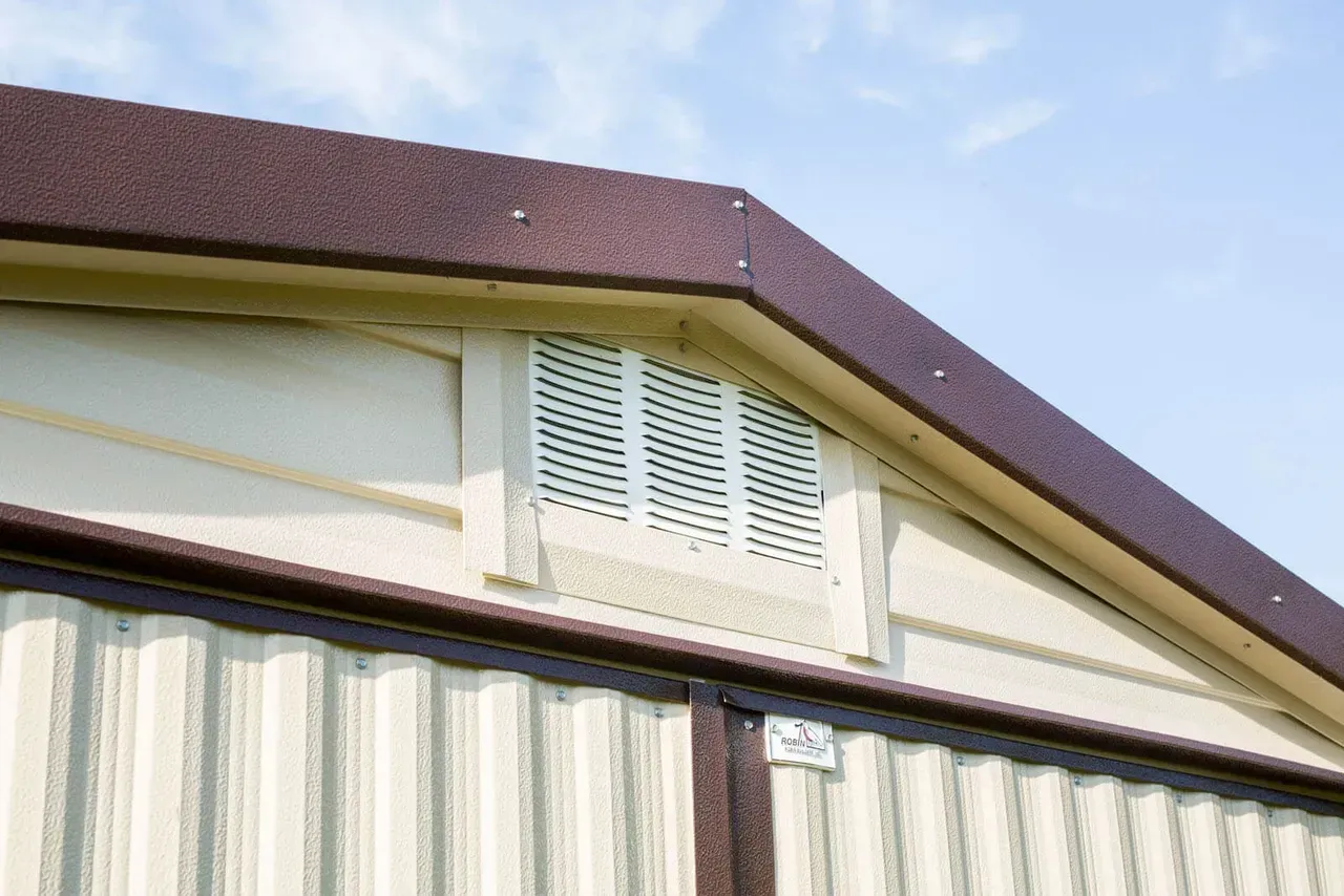 A portion of a building with a dark brown roof and beige siding, featuring a vent.