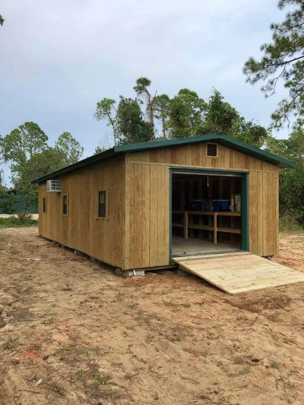 Wooden shed with a ramp, a green roof, and an open garage door.