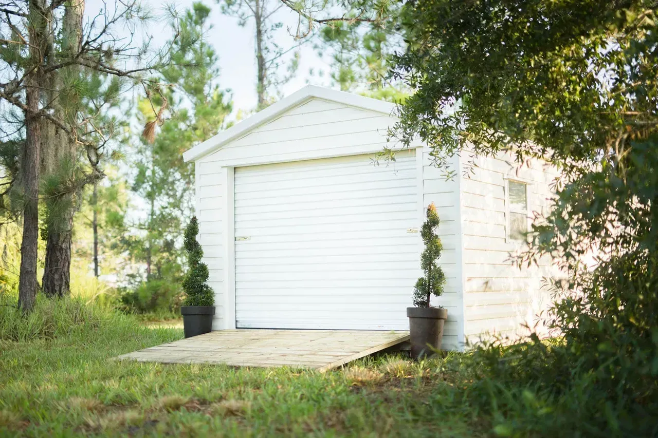 White garage with a sloped wooden entrance and potted topiary.