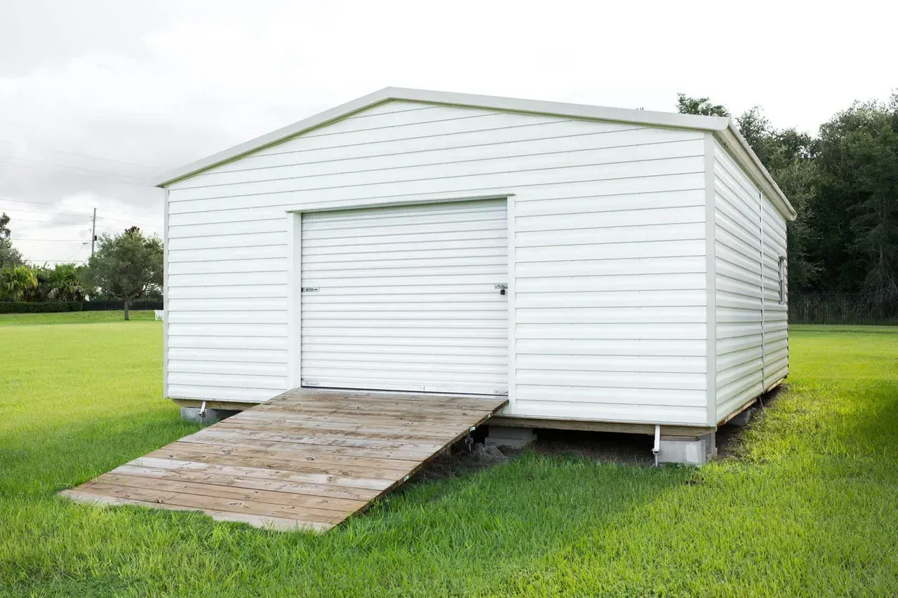 White shed with a wooden ramp on a grassy lawn.